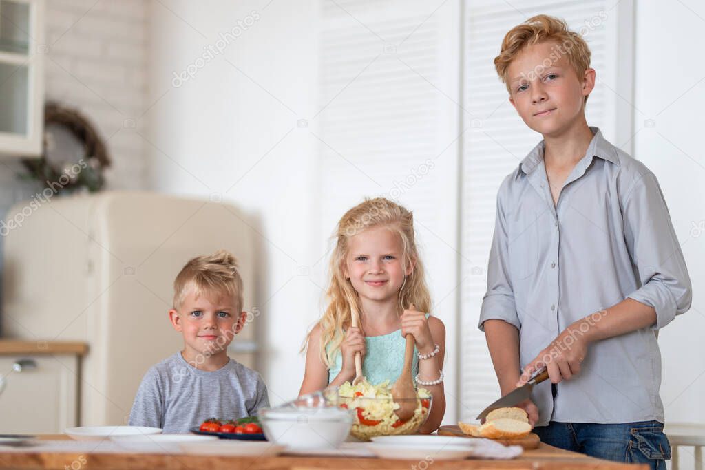 three blonde kids twoboys and girl on kitchen at home. Family eating healthy food , green salad on plates. Looking at camera