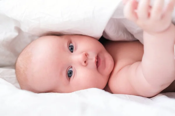 Adorável menino sorridente sob cobertor branco no quarto. Recém-nascido relaxando na cama. Manhã de família em casa. Crianças recém-nascidas — Fotografia de Stock