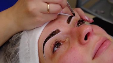 Güzellik salonunda kalın kaşlı bir kadının kalıcı makyajı için. Yakından bir güzellik uzmanı boyama dövmesi yaptırıyor.