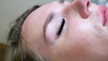 Kirpik uzatma prosedürünü kapat. Kirpik uzatma ustası güzellik salonundaki kadın müşteriye uzun yapay kirpikler yapıştırıyor. 4k görüntü