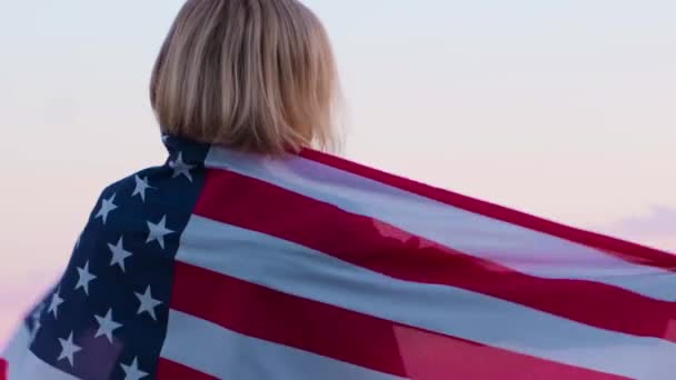 4k.Vissza nézet nő nyári ruhákban nemzeti amerikai zászló szabadban óceán naplemente - amerikai zászló, ország, hazafiság, függetlenség napja és az emberek koncepció. — Stock videók