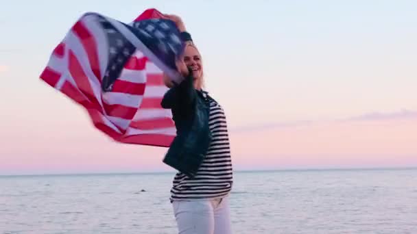 4k. feliz mujer sonriente en ropa de verano con bandera nacional de EE.UU. al aire libre puesta de sol del océano - bandera estadounidense, país, patriotismo, día de la independencia y el concepto de la gente . — Vídeos de Stock