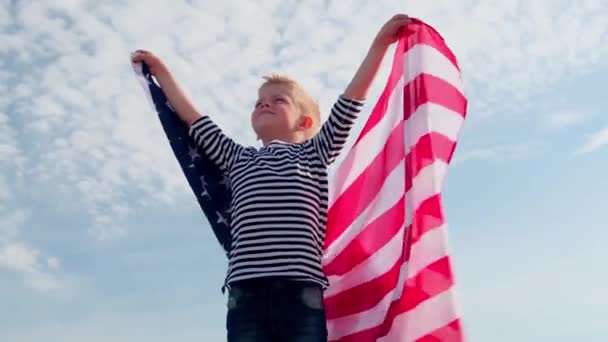 4k. Niño rubio ondeando bandera nacional de EE.UU. al aire libre sobre el cielo azul en verano bandera americana, país, patriotismo, día de la independencia 4 de julio . — Vídeos de Stock