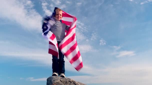 4K. Menino loiro acenando bandeira nacional dos EUA ao ar livre sobre o céu azul no verão bandeira americana, país, patriotismo, dia da independência 4 de julho . — Vídeo de Stock