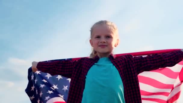 4K. Menina loira acenando bandeira nacional dos EUA ao ar livre sobre o céu azul no verão bandeira americana, país, patriotismo, dia da independência 4 de julho . — Vídeo de Stock
