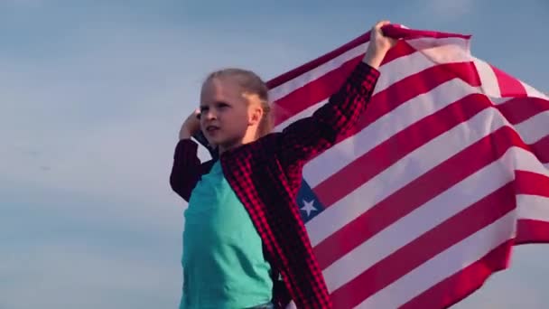 4k. Chica rubia ondeando bandera nacional de EE.UU. al aire libre sobre el cielo azul en verano bandera americana, país, patriotismo, día de la independencia 4 de julio . — Vídeos de Stock