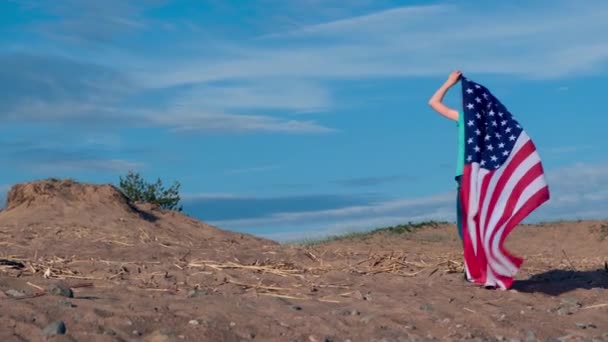 4K. Voltar vista menina andando e acenando bandeira nacional dos EUA ao ar livre sobre o céu azul no verão bandeira americana, país, patriotismo, dia da independência 4 de julho . — Vídeo de Stock