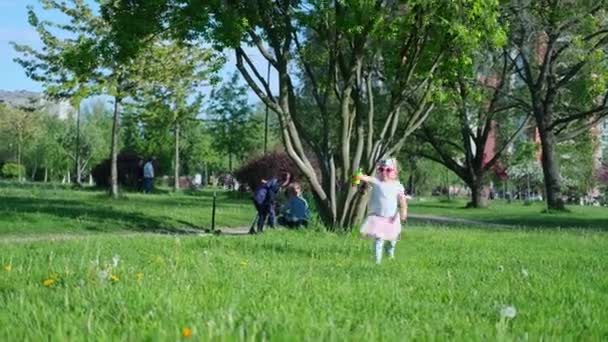 4kだ。夏に緑の公園を走るかわいい赤ちゃんの女の子。楽しい屋外で遊んで幸せな子供。ピンクのスカートと眼鏡。サンクトペテルブルクロシア2020年6月4日 — ストック動画