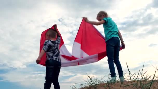 4k. Kleine jongen en meisje hebben plezier in het inpakken van nationale Canada vlag buiten boven de blauwe lucht in de zomer - Canada dag, land, patriottisme, onafhankelijkheidsdag 1 juli — Stockvideo
