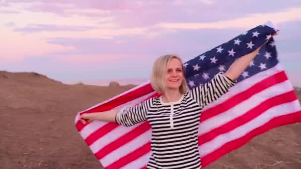 4k. gelukkig glimlachende vrouw in de zomer kleding met nationale VS vlag buiten oceaan zonsondergang - Amerikaanse vlag, land, patriottisme, onafhankelijkheidsdag en mensen concept. — Stockvideo