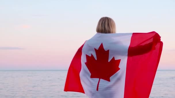 4k.Back view vrouw in de zomer kleding met nationale canada vlag buiten oceaan zonsondergang - Canada vlag, land, patriottisme, onafhankelijkheid dag en mensen concept. — Stockvideo