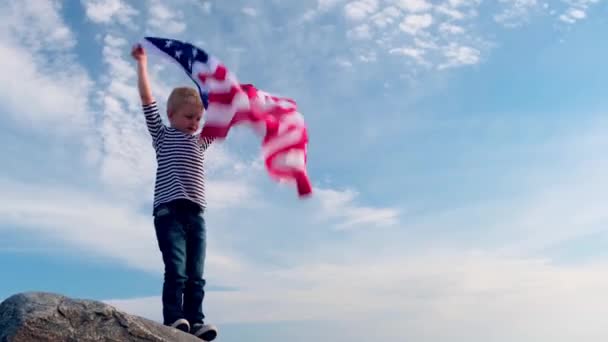 4k. Blond pojke viftar nationell USA flagga utomhus över blå himmel på sommaren - amerikansk flagga, land, patriotism, självständighetsdagen 4 juli. — Stockvideo
