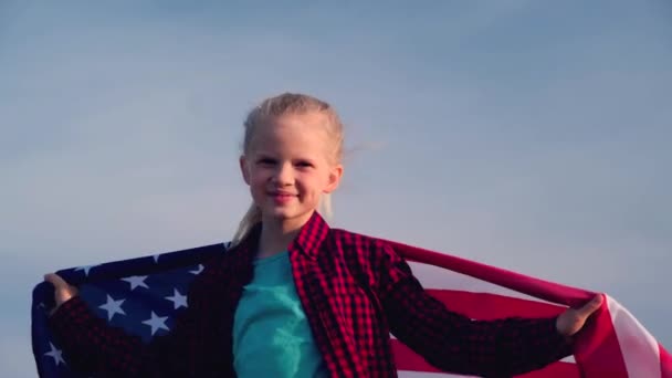 4K. Menina loira acenando bandeira nacional dos EUA ao ar livre sobre o céu azul no verão bandeira americana, país, patriotismo, dia da independência 4 de julho . — Vídeo de Stock