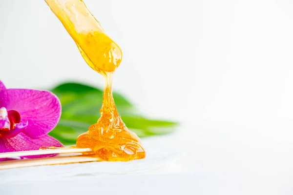 Pasta de azúcar o miel de cera para eliminar el cabello fluye hacia abajo de palitos de espátula de cera de madera. fondo de flores - depilación y concepto de belleza. copyspase —  Fotos de Stock