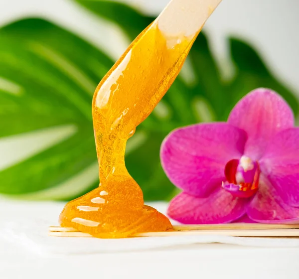 Pasta de azúcar o miel de cera para eliminar el cabello fluye hacia abajo de palitos de espátula de cera de madera. fondo de flores - depilación y concepto de belleza —  Fotos de Stock