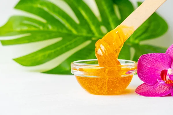 Pasta de azúcar o miel de cera para eliminar el cabello fluye hacia abajo de palitos de espátula de cera de madera. fondo de flores - depilación y concepto de belleza. copyspase —  Fotos de Stock