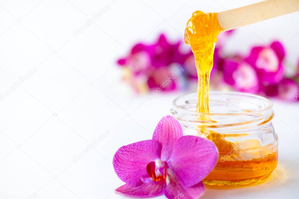 sugar paste or wax honey for hair removing flows down from wooden waxing spatula sticks. flower background - depilation and beauty concept