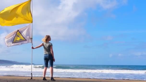 Back view girl holding yellow flag warning weather wind on beach at ocean coastline 22 nov 2019 Canarian Island Spain — Αρχείο Βίντεο