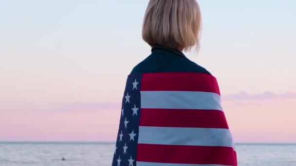 4k.Back view vrouw in de zomer kleding met nationale VS vlag buiten oceaan zonsondergang - Amerikaanse vlag, land, patriottisme, onafhankelijkheidsdag en mensen concept. — Stockvideo