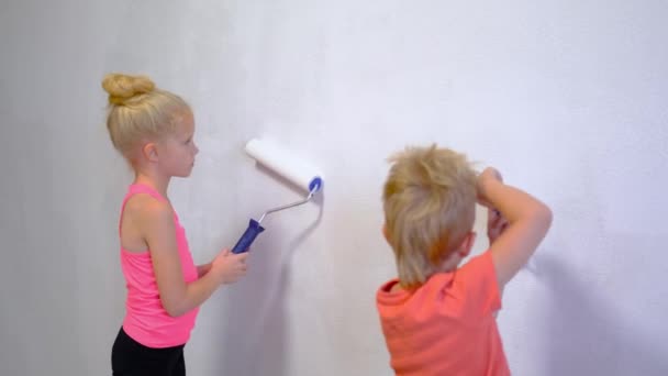 4K. menino loiro e menina fazendo reparos em casa, irmão e irmã pintura pintura rolo parede tinta branca. Renovação, interior da família . — Vídeo de Stock