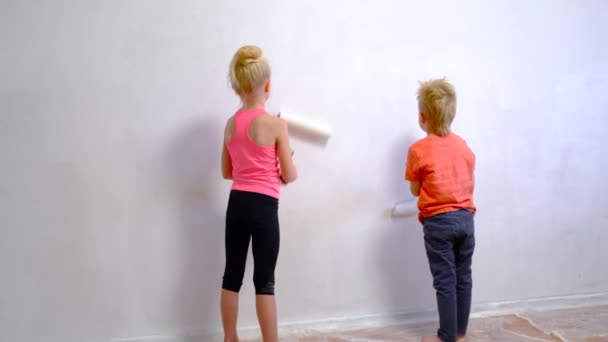 4k. biondo ragazzo e ragazza fare le riparazioni a casa, fratello e sorella pittura rullo muro vernice bianca. Ristrutturazione, arredamento familiare. — Video Stock