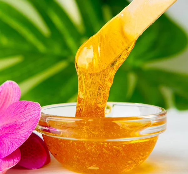 Pasta de azúcar o miel de cera para eliminar el cabello fluye hacia abajo de palitos de espátula de cera de madera. fondo de flores - depilación y concepto de belleza —  Fotos de Stock