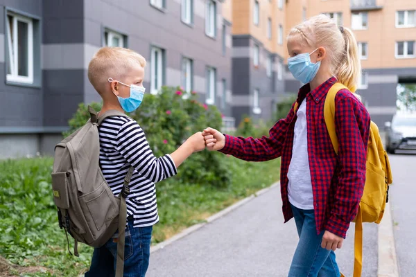 Çocuklar selamlıyor. Maske takan ve sırt çantası takan çocuklar okula dönmek için koronavirüsü koruyorlar. Bou ve kız salgından sonra okula gidiyorlar.. 