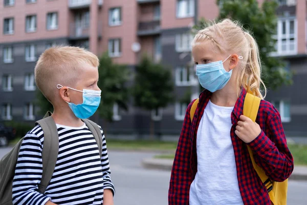 Maske takan ve sırt çantası takan çocuklar okula dönmek için koronavirüsten korunup korunuyorlar. Erkek ve kız kardeş salgından sonra okula gidiyor. Öğrenciler yeni okul yılı için hazır.