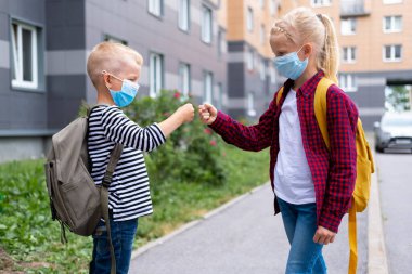 Çocuklar selamlıyor. Maske takan ve sırt çantası takan çocuklar okula dönmek için koronavirüsü koruyorlar. Bou ve kız salgından sonra okula gidiyorlar.. 