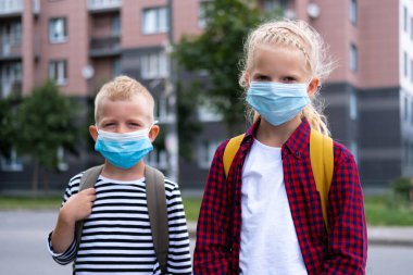Maske takan ve sırt çantası takan çocuklar okula dönmek için koronavirüsten korunup korunuyorlar. Erkek ve kız kardeş salgından sonra okula gidiyor. Kamera öğrencileri yeni okul yılına hazırlar.