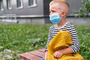 Okula dönüyorum. Maske ve sırt çantası takan Mutlu Çocuk, koronavirüsten korunuyor ve güvende. Çocuk salgın bittikten sonra okulun yanında oturuyor. Öğrenciler yeni yıla hazır.