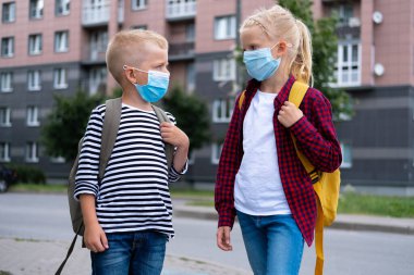 Maske takan ve sırt çantası takan çocuklar okula dönmek için koronavirüsten korunup korunuyorlar. Erkek ve kız kardeş salgından sonra okula gidiyor. Öğrenciler yeni okul yılı için hazır.