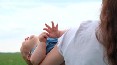 4 bin. Küçük çocuk gülümsüyor, gülüyor ve kameraya bakıyor. Annem yazın bebeği mavi bulutlu gökyüzünün üzerinde tutuyor. Mutlu çocukluk ve aile kavramı.