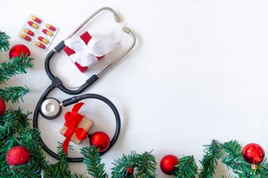 İçinde haplar, hediye kutusu, steteskop ve beyaz ahşap arka planda Noel ağacı olan tıbbi afiş. Kopyalama. Tıbbın yeni yılı