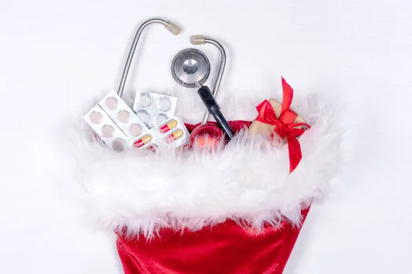 Medicinskt julkort med piller, presentförpackning, stetoskop på vit trä bakgrund. Kopieringsutrymme. Medicin nytt år platt — Stockfoto