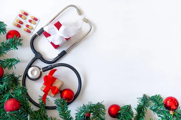 İçinde haplar, hediye kutusu, steteskop ve beyaz ahşap arka planda Noel ağacı olan tıbbi afiş. Kopyalama. Tıbbın yeni yılı