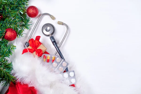 Medical banner with pills, gift present box, stethoscope and Christmas tree on white wooden background. Copyspace. Medicine new year flatly