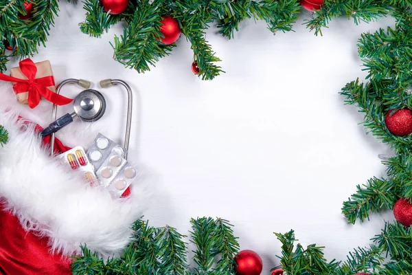 Medical banner with pills, gift present box, stethoscope and Christmas tree on white wooden background. Copyspace. Medicine new year flatly