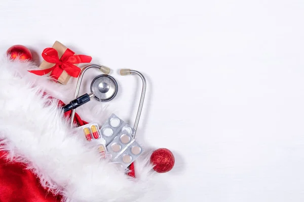 Medyczna kartka świąteczna z pigułkami, pudełko prezentów, stetoskop na białym drewnianym tle. Przestrzeń kopiowania. Medycyna Nowy Rok płasko — Zdjęcie stockowe