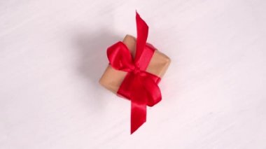 Pembe ahşap arka planda dönen kırmızı kurdeleli hediye kutusu. 360 derece dönüş. Kusursuz döngü. Konsept satışlar, indirimli fiyatlar, Noel tatilleri ve alışveriş.