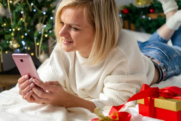 Świąteczne zakupy online. Kupiec składa zamówienie na telefon komórkowy. Kobieta kupuje prezenty, przygotowuje się do świąt, pudełko z prezentami w ręku. Sprzedaż wakacji zimowych — Zdjęcie stockowe