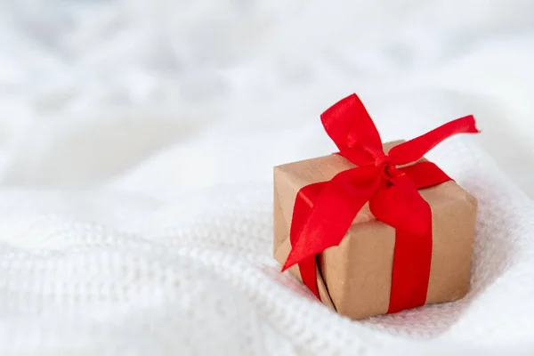 Beyaz örgü süveter arka planında hediye kutusu kırmızı kurdele olan Noel kartı. Kopyalama alanı — Stok fotoğraf