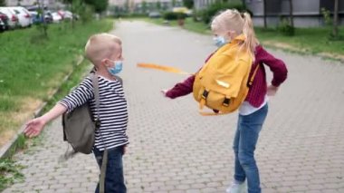 Okula dört bin dolar. Çocuklar sokakta oynuyor. Maske takan ve sırt çantası takan çocuklar koruma ve güvenlik koronavirüsü. Oğlan ve kız salgın hastalık üstüne okula gidiyorlar.. 