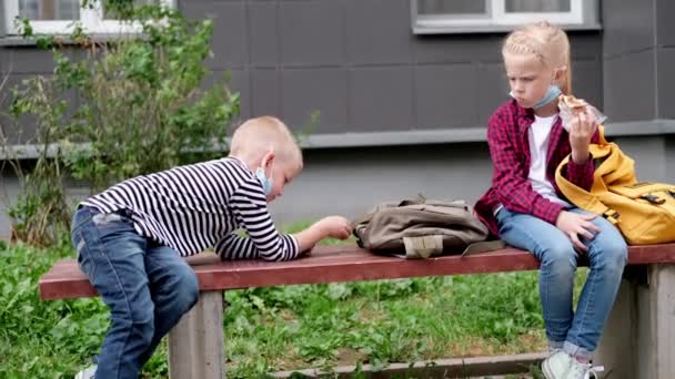 4Kは学校に戻る。女の子と男の子子供は学校の近くのベンチで話して座っているマスクを身に着けている社会的距離を保つ — ストック動画
