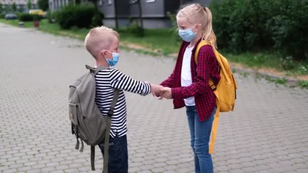 4Kは学校に戻る。子供たちはバックパックを持って街で遊んでいます。マスク安全コロナウイルスを身に着けている子供たち。大流行の後に学校に行く男の子と女の子. — ストック動画