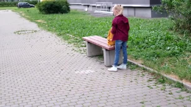 4k tillbaka visa blond flicka sätter böcker i sin ryggsäck på gatan nära skolan — Stockvideo