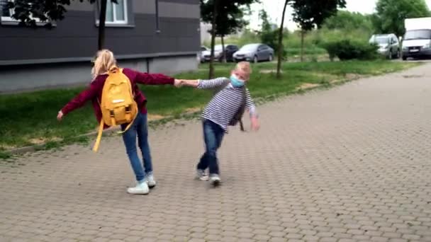 4k torna a scuola. bambini che giocano per strada. I bambini che indossano maschera e zaini proteggono e sicurezza coronavirus. Ragazzo e ragazza andare a scuola dopo pandemia oltre. — Video Stock