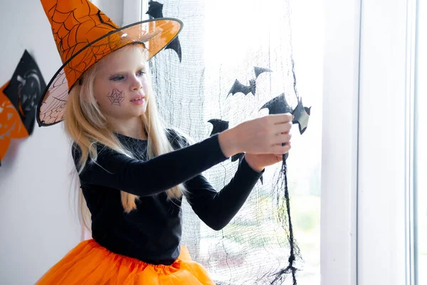 Happy girl in witch costume preparing for Halloween Decorating window in room by black bats — Stock Photo, Image