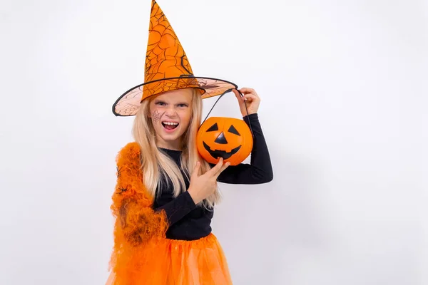 Emocionado niña rubia en traje de bruja con cubo de caramelo de calabaza de Halloween en el fondo del estudio blanco. espacio de copia —  Fotos de Stock