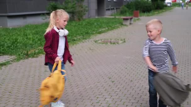 4k πίσω στο σχολείο. παιδιά που παίζουν στο δρόμο, ξανθό αγόρι και κορίτσι που στριφογυρίζουν με σακίδια. — Αρχείο Βίντεο